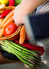 Nahaufnahme eines Einkaufkorbs mit verschiedenen Gemüsesorten, darunter Möhren, Kartoffeln und Spargel. 